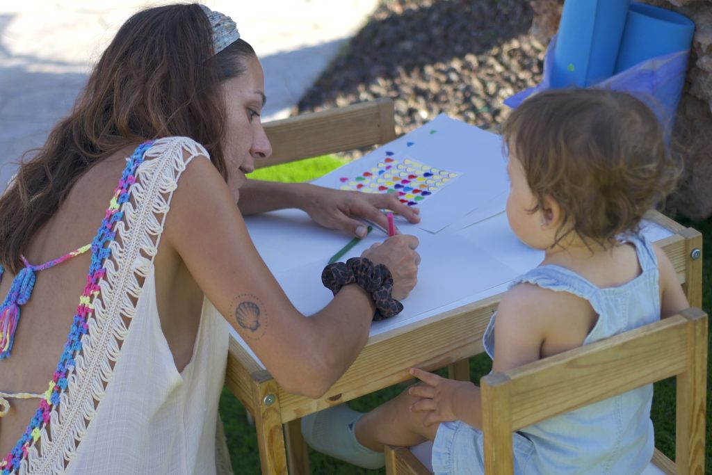 Una dona i una nena petita fent manualitats amb adhesius i llapis a l’exterior de la Masia L’Encís
