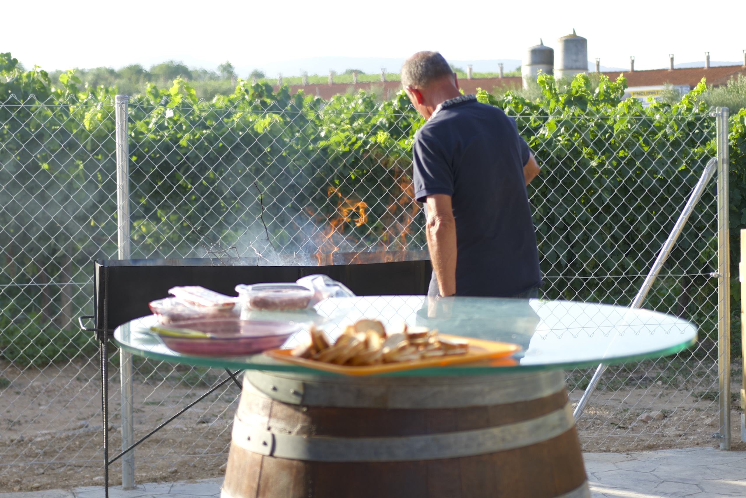 Home preparant una barbacoa entre vinyes a la Masia L’Encís, amb menjar a punt de servir