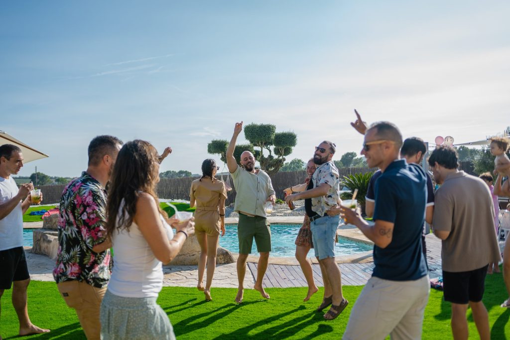 Grup d’amics ballant i gaudint d’una festa d’estiu a la piscina de Masia L’Encís en un entorn natural