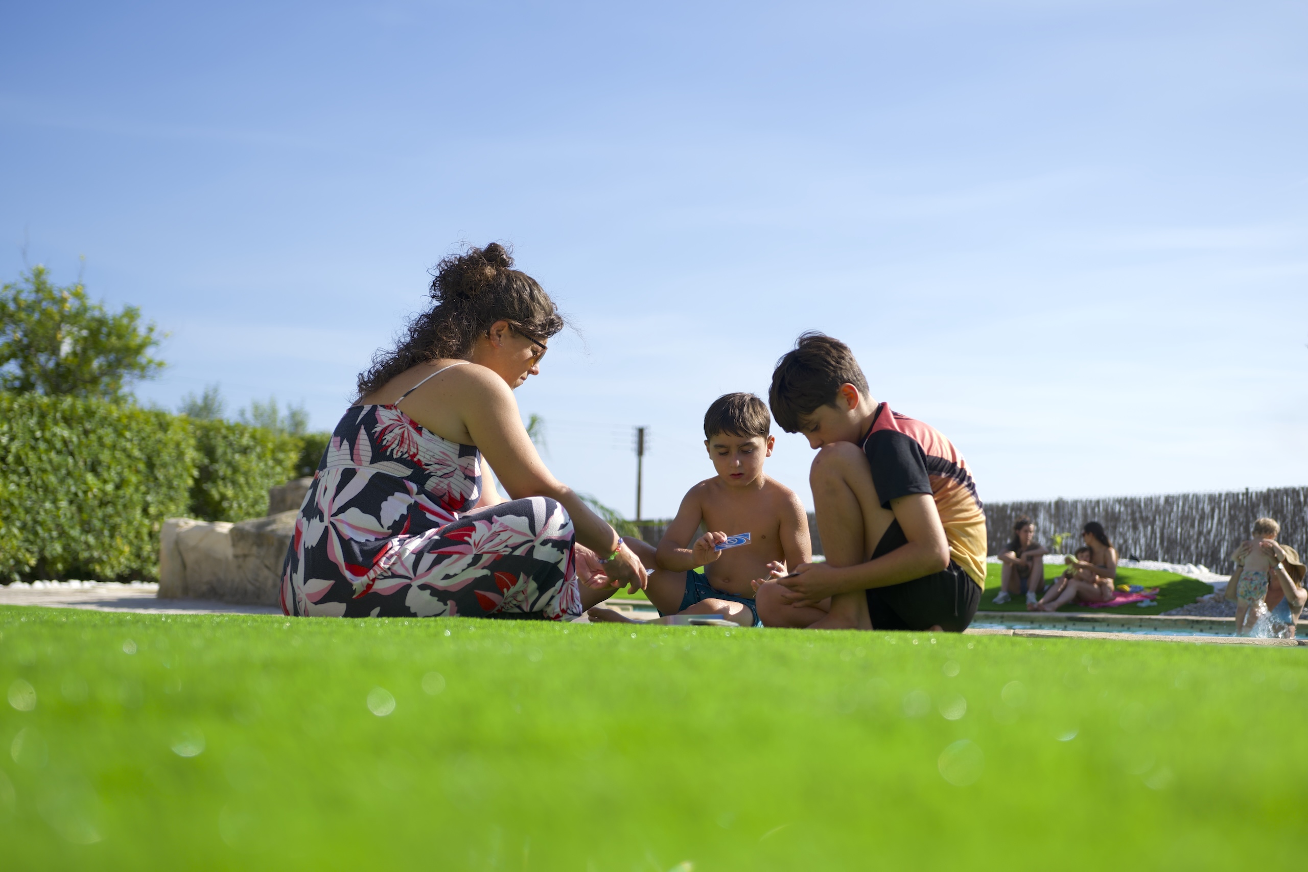 Família jugant amb nens a la gespa de la Masia L’Encís, en un ambient tranquil i estiuenc