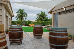 Espai exterior amb botes de fusta reutilitzades com a taules a la Masia L’Encís, amb vistes al jardí i piscina