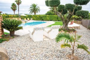 Butaques de mosaic davant la piscina de la Masia L’Encís, envoltades de jardí i vegetació mediterrània