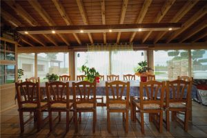 Menjador interior de la Masia L’Encís amb taula llarga, cadires de fusta i sostre de bigues