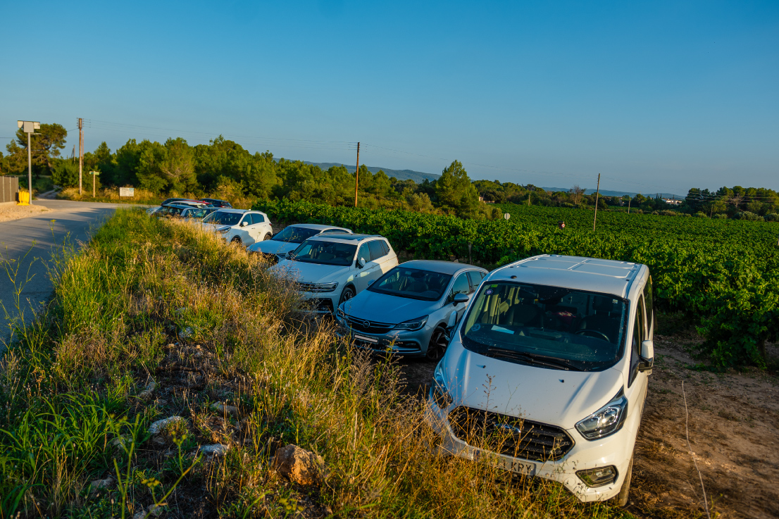 Zona d’aparcament de la Masia L’Encís amb cotxes estacionats entre vinyes i natura