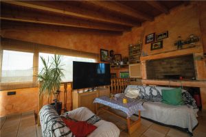 Sala d’estar interior de la Masia L’Encís amb sofàs, televisió, sostre de fusta i decoració acollidora