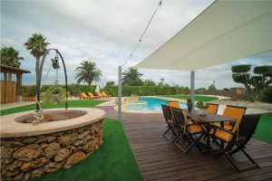 Taula exterior amb cadires i ombra a la Masia L’Encís, amb vistes a la piscina i jardí