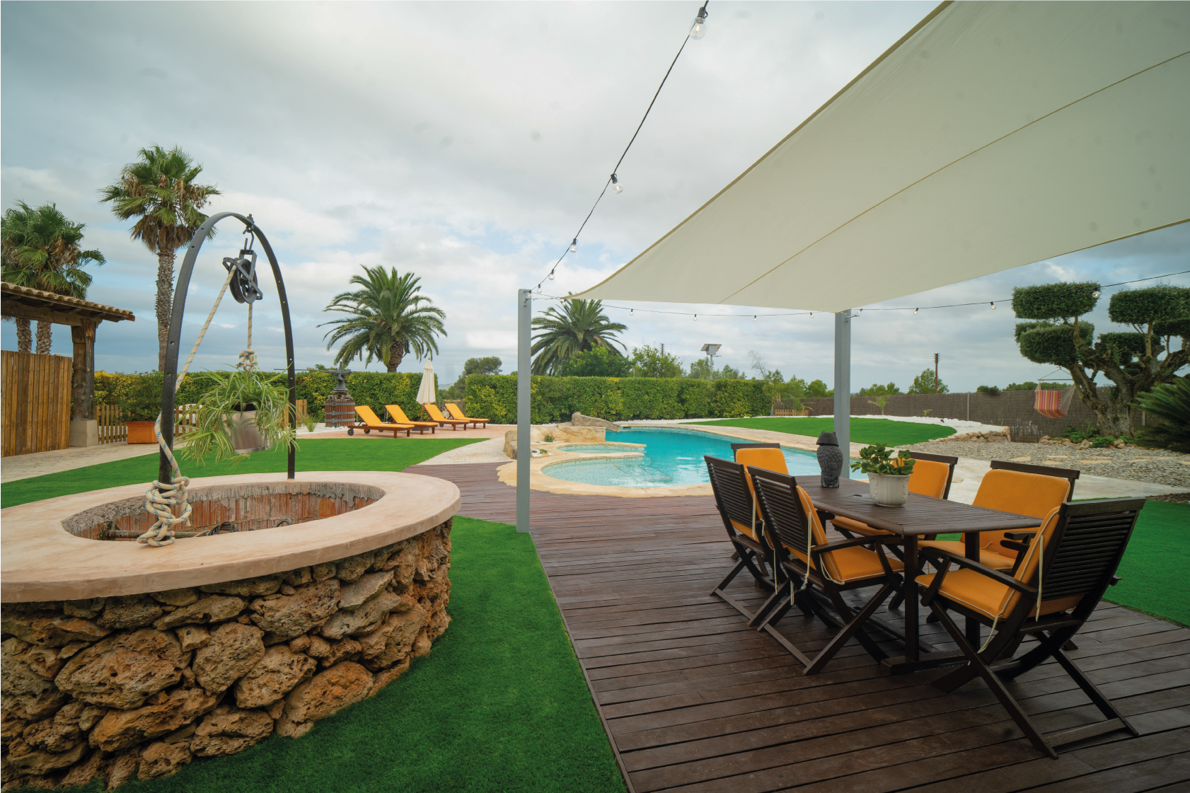 Taula exterior amb cadires i ombra a la Masia L’Encís, amb vistes a la piscina i jardí