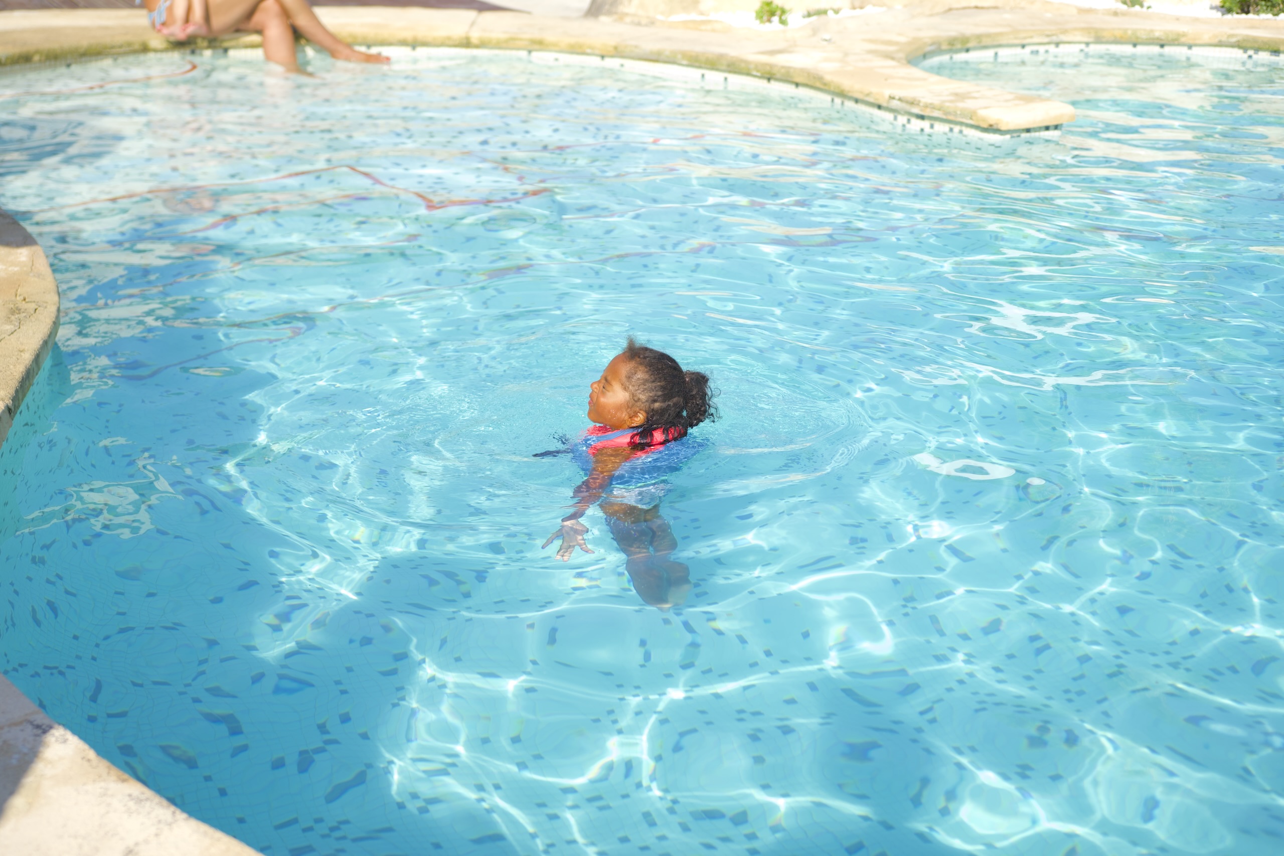 Nena petita amb flotador jugant feliç a la piscina de la Masia L’Encís en un dia d’estiu